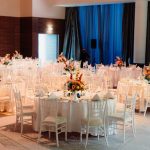 White banquet chairs with tables decorated with matching floral centerpieces