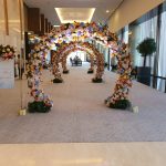 Wedding entrance with multiple floral archways and chandeliers along a hotel corridor