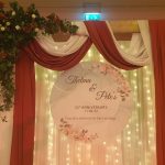25th anniversary backdrop with floral signage, draped fabric, and warm fairy lights