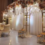 Wedding stage with chandeliers, floral canopy arches, lanterns, and a classic ivory loveseat