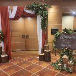 Rustic wedding entrance setup with draped fabric, lanterns, floral decor, and a wooden welcome sign