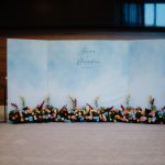 Wedding photo wall backdrop with pastel blue-sky design and floral arrangements at the base